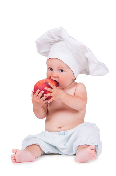 A small child is eating a big peach in a chef suit on a white background. - Foto, immagini