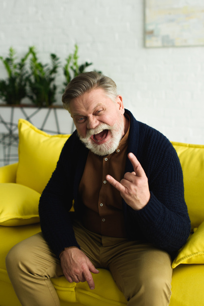 excited bearded senior man showing rock gesture and screaming at camera - Photo, image