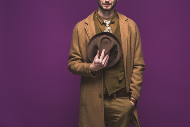 Stylish man wearing coat and holding hat isolated on purple - Fotoğraf, Görsel