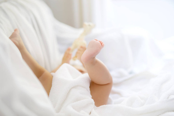 Bebé bonito brincando com os próprios pés depois de tomar banho. Adorável menina bonita envolto em toalhas brancas
 - Foto, Imagem
