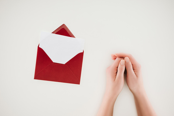 обрезанный снимок женщины, держащейся за руки рядом с открытым красным конвертом с чистой бумагой, изолированной на белом
 - Фото, изображение