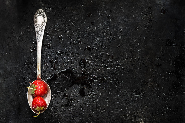σε ένα κουτάλι μια υγρή φράουλα σε σκούρο φόντο με πιτσιλιές o - Φωτογραφία, εικόνα