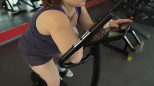 Obese woman having labored breathing, sitting on stationary bike in the gym - Filmmaterial, Video