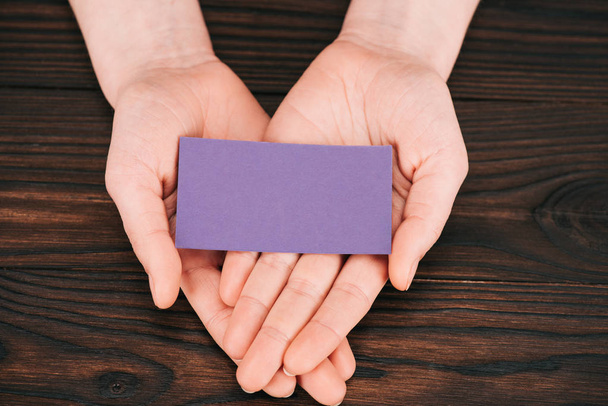 cropped shot of woman holding blank purple paper over wooden table - Photo, Image