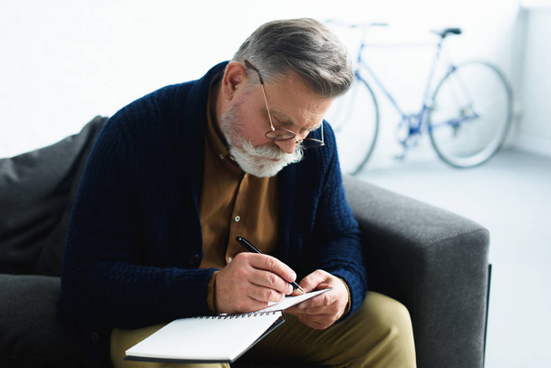 зосереджений старший чоловік в окулярах робить нотатки на блокноті
 - Фото, зображення