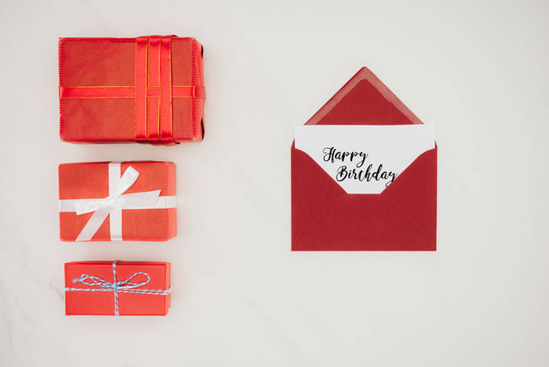 pohled shora červené obálky s nápisem Happy Birthday na papíře a řada dárkových krabiček izolované na bílém - Fotografie, Obrázek