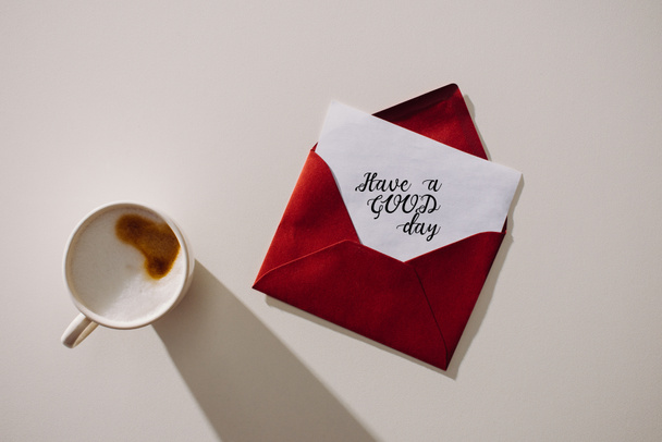 Widok z góry z czerwoną kopertę z mieć dobry dzień napis napis na papier i filiżankę kawy - Zdjęcie, obraz