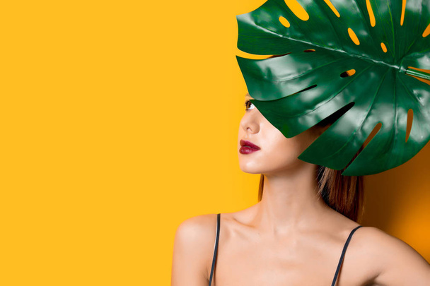 Beautiful woman in dark clothes with palm leaf on yellow color background - Фото, зображення