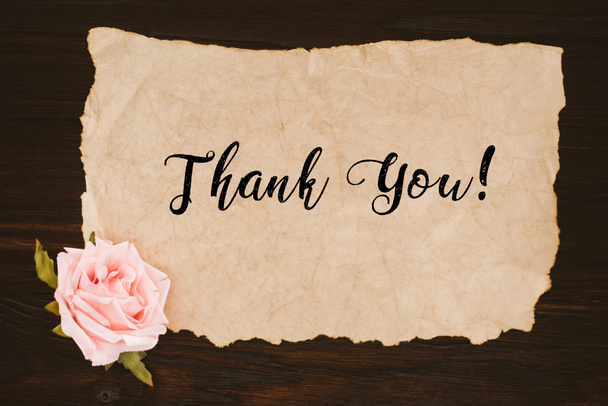 top view of aged paper with thank you lettering and rose flower on wooden table - Photo, Image
