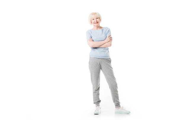 Sportive senior souriante debout avec les bras croisés isolés sur blanc
 - Photo, image