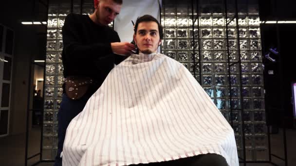 der Friseur schneidet den jungen Mann und spricht ihn an - Filmmaterial, Video