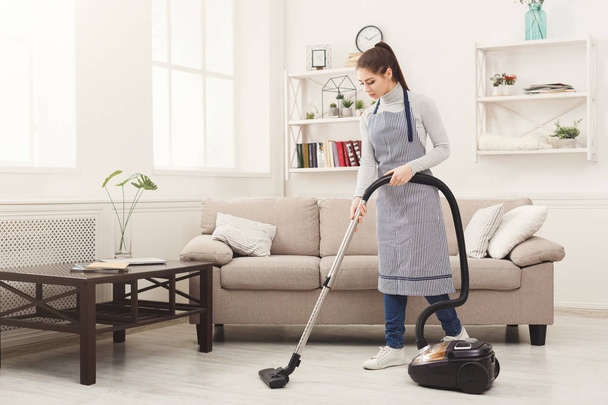 Nuori nainen puhdistaa talon pölynimurilla
 - Valokuva, kuva