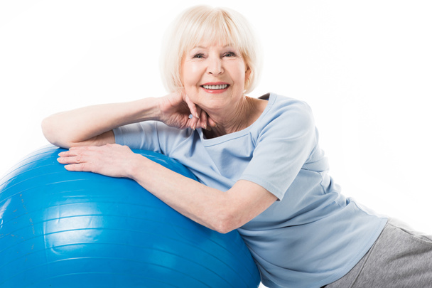Портрет улыбающейся старшей спортсменки с изолированным на белом мячом для фитнеса
 - Фото, изображение