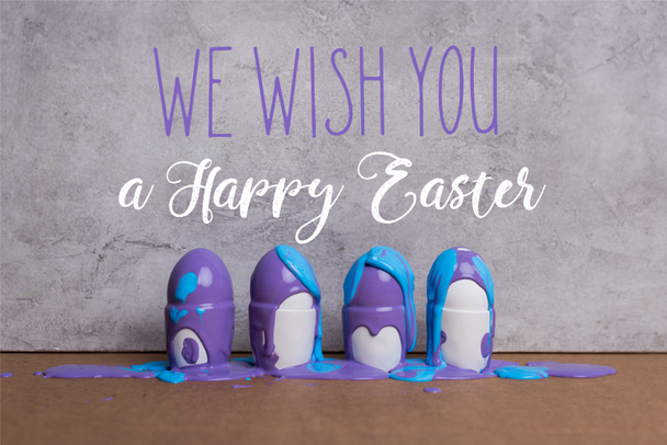 Paint covering eggs in cups with we wish you happy easter lettering on grey background - Photo, Image