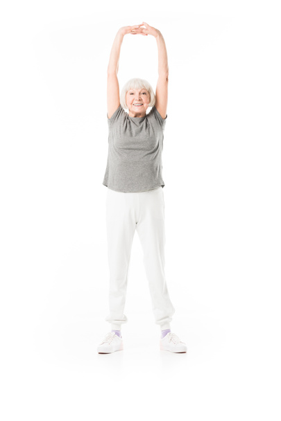 Smiling senior sportswoman with arms up doing excercise isolated on white - Фото, изображение