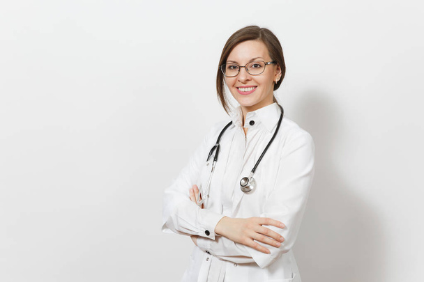 Smiling confident beautiful young doctor woman with stethoscope, glasses isolated on white background. Female doctor in medical gown holds hands folded. Healthcare personnel, health, medicine concept. - Photo, Image