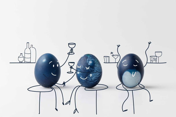 three blue painted easter eggs with drawn faces drinking at bar on white surface - Foto, Imagem