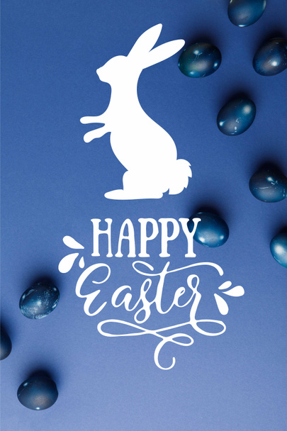 верхний вид голубых окрашенных пасхальных яиц со счастливой надписью Пасхи и силуэтом кролика на голубой поверхности
 - Фото, изображение