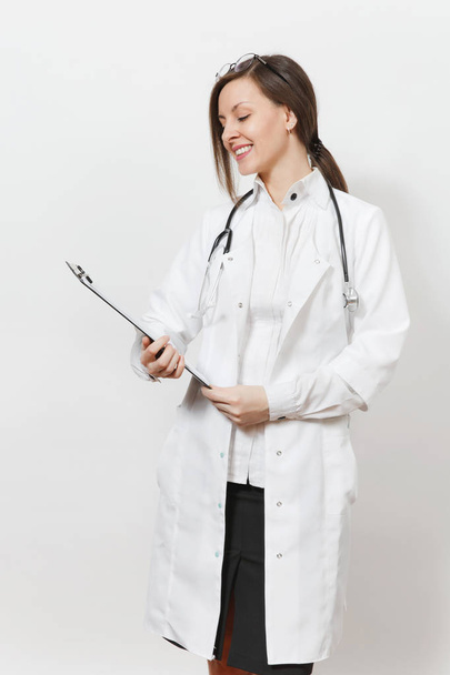 Lächelnde, selbstbewusste junge Ärztin mit Stethoskop, Brille auf weißem Hintergrund. Ärztin im Arztkittel mit Gesundheitskarte auf dem Notizblock. Konzept für medizinisches Personal. - Foto, Bild