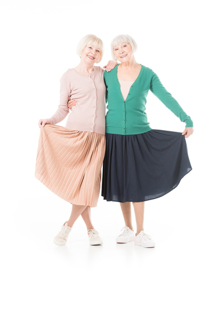 Retrato de sorrir mulheres seniores elegantes segurando saias isoladas em branco
 - Foto, Imagem