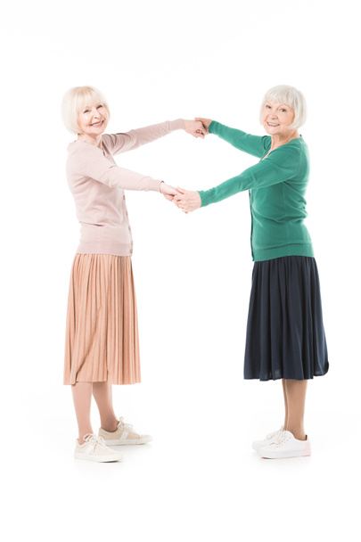 zwei stylische Seniorinnen, die einander die Hand reichen, isoliert auf weißem Grund - Foto, Bild