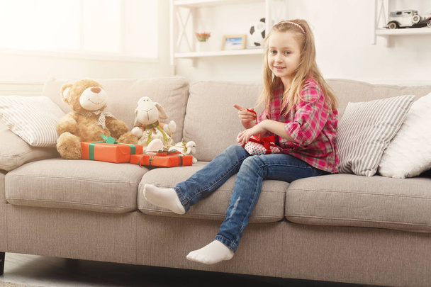 Όμορφο μικρό κορίτσι upwrapping παρουσιάζει στον καναπέ στο σπίτι - Φωτογραφία, εικόνα