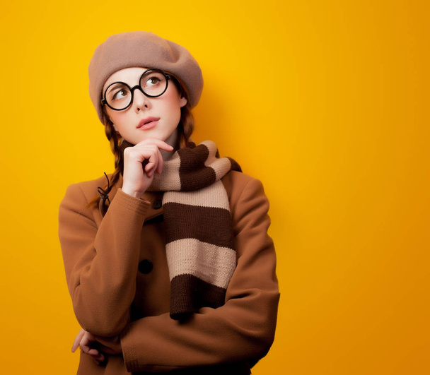 Портрет юной зануды в пальто и очках на жёлтом фоне
  - Фото, изображение