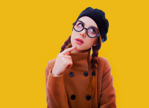 Portrait d'une jeune rousse drôle de nerd fille avec des lunettes et un manteau sur fond jaune
 - Photo, image