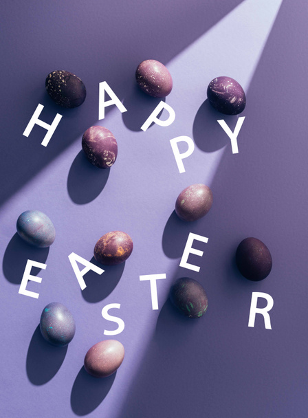 Easter purple eggs with happy easter lettering on purple background with sunbeam - Photo, Image