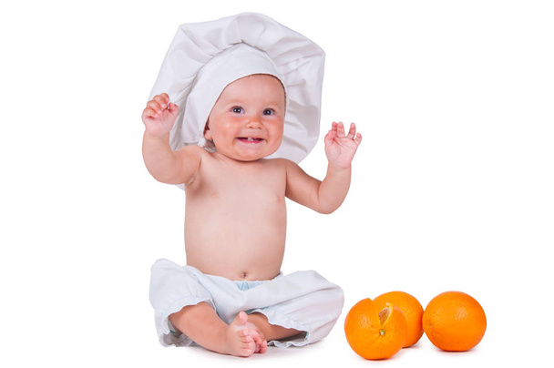 Małe dziecko zje plasterek pomarańczy w garniturze kucharz na białym tle. - Zdjęcie, obraz