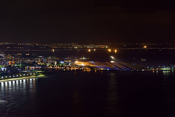 Nacht uitzicht op de top van de Santos Dumont luchthaven in het centrum van Rio de Janeiro met verlichting, gebouwen en Rio Niteroi brug op de achtergrond - Foto, afbeelding
