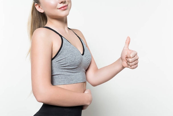 Close-up view of young woman in sports top showing thumb up isolated on white - 写真・画像