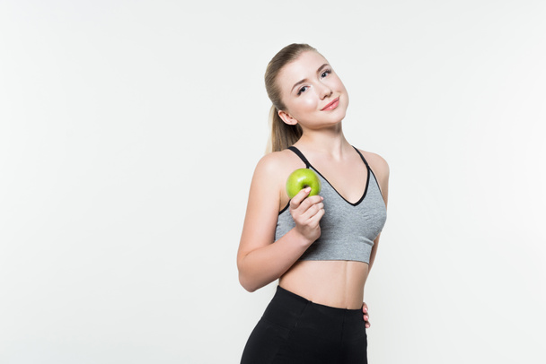 Молодая женщина в спортивном топе держит яблоко изолировано на белом
 - Фото, изображение