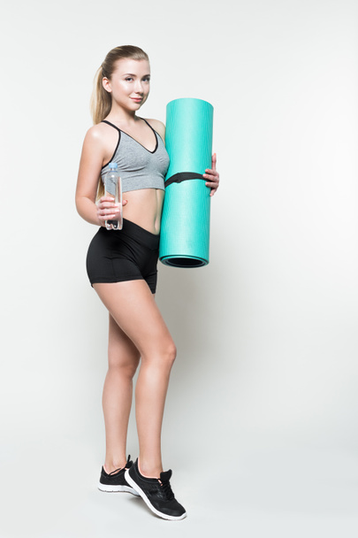 Sportswoman holding water bottle and yoga mat isolated on white - Photo, Image