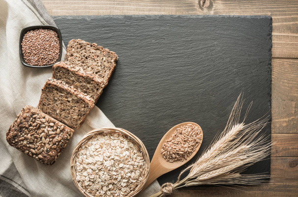 Fitness bread. A loaf of fresh rustic whole rye bread with wheat, sliced on a black slate dish and board, rural food background. Top view. Copy space. - Foto, Bild