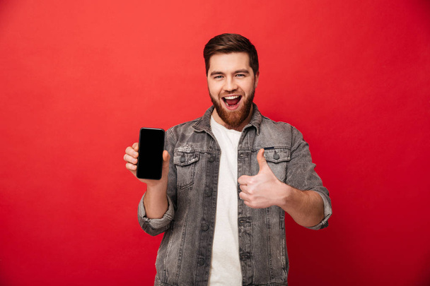 Image of unshaved happy man showing cell phone on camera and ges - Fotografie, Obrázek