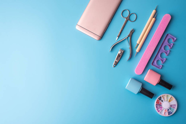 A set of cosmetic tools for manicure and pedicure on a blue background. Gel polishes, nail files and clippers, top view - 写真・画像