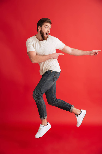 Emotional bearded man jumping pointing to copyspace. - Foto, afbeelding