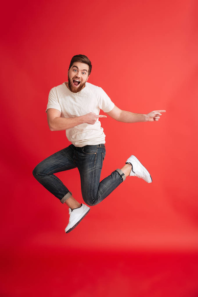 Emotional bearded man jumping pointing to copyspace. - Photo, Image