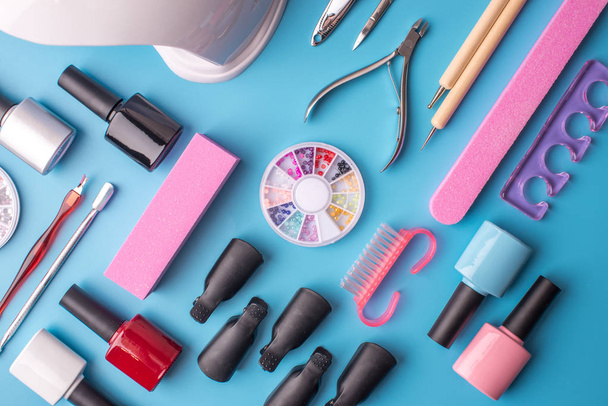 Conjunto de herramientas cosméticas para manicura y pedicura sobre fondo azul. Esmaltes de gel, limas y cortauñas, vista superior
 - Foto, imagen