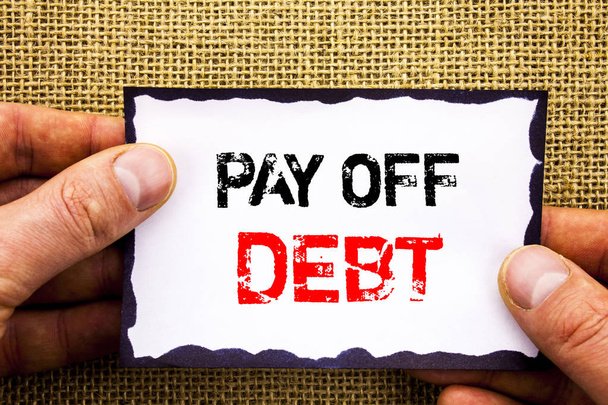 Writing text showing  Pay Off Debt. Concept meaning Reminder To Paying Owed Financial Credit Loan Bills written on Sticky Note Paper Holding Hand with Finger. - Photo, Image