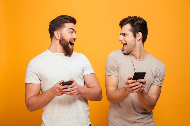 Portrait of a two happy young men holding mobile phones - Foto, afbeelding