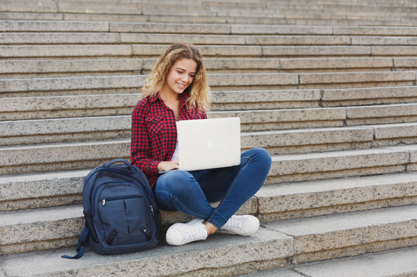 Opiskelija istuu portaissa ja työskentelee kannettavan tietokoneen kanssa ulkona
 - Valokuva, kuva