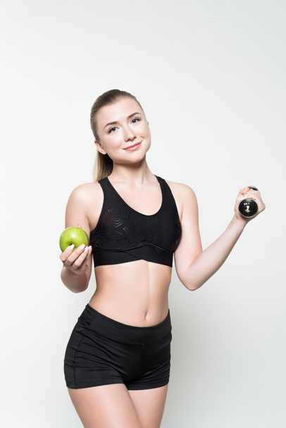 Young woman in sports top holding dumbbell and apple isolated on white - Φωτογραφία, εικόνα