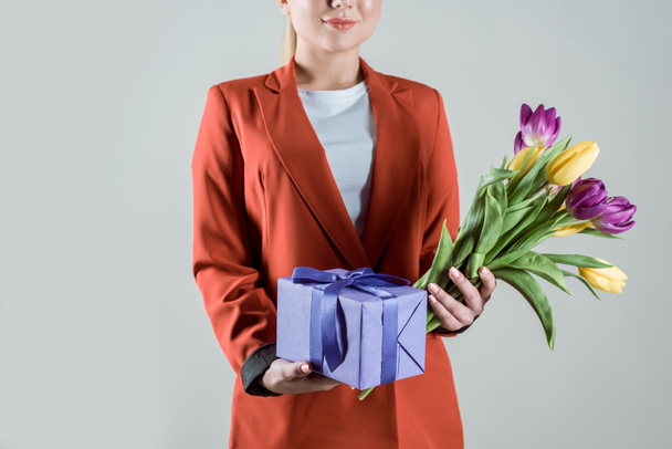 Gift box and tulips bouquet in hands of stylish woman isolated on grey - Photo, Image