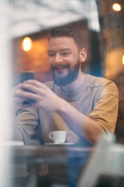 Jeune homme assis dans un café et utilisant un téléphone intelligent
. - Photo, image