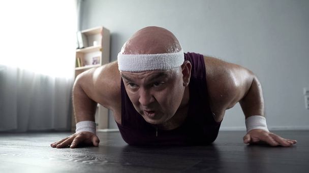 Sweating male with weak arm muscles trying to do push-ups at home, workout - Photo, Image