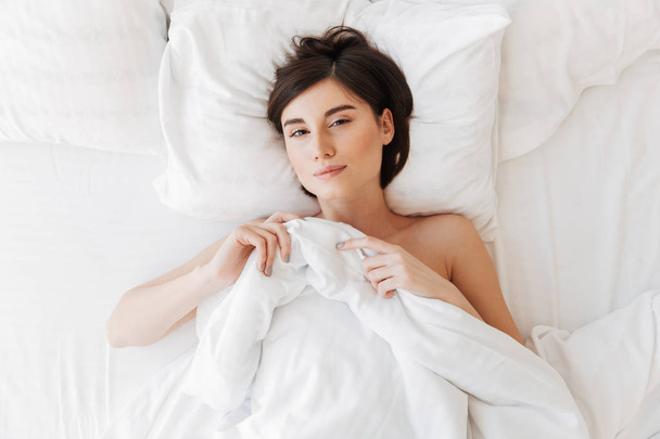 Bovenaanzicht portret van een slaperig jonge vrouw in bed liggen - Foto, afbeelding