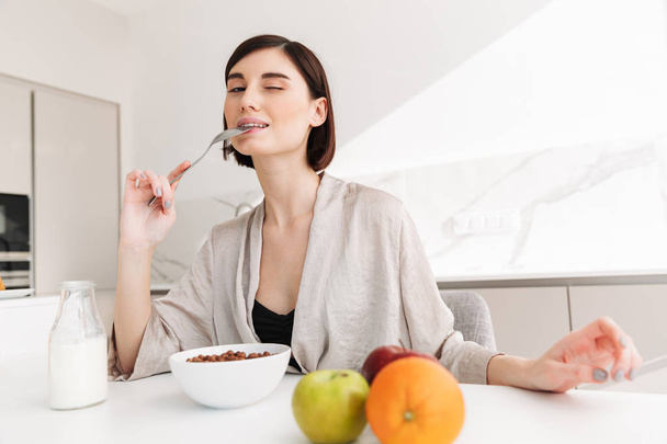 Photo of joyful young woman having breakfast in kitchen of hotel - Foto, imagen