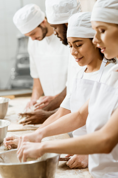 grupo de panaderos multiétnicos amasando masa juntos
 - Foto, Imagen